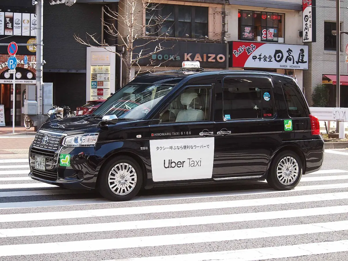 Tokyo taxi with an Uber Taxi sign on the door, crossing a city street
