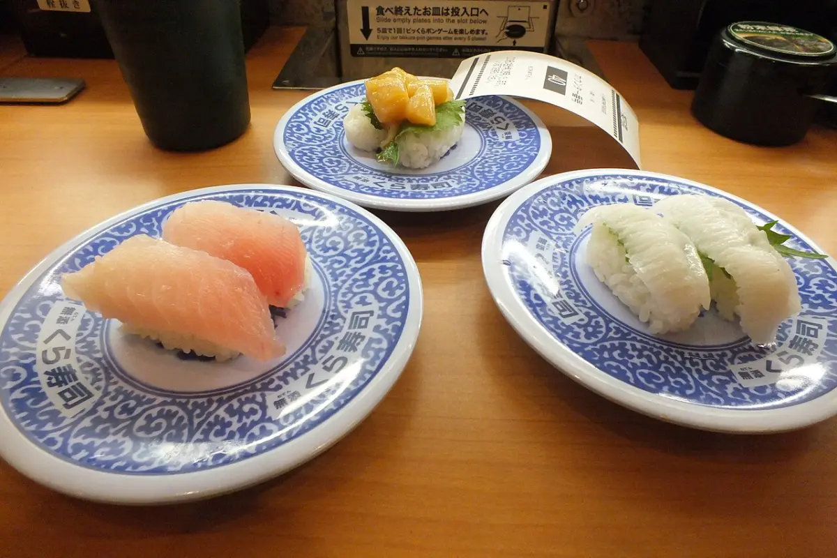 Nigiri sushi on blue Kura Sushi plates, with the plate return slot on the table behind