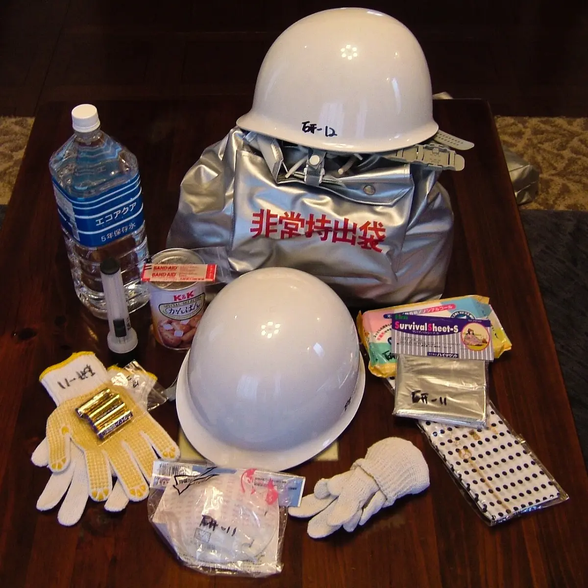 Japanese emergency kit with helmets, water, gloves and an emergency bag laid out on a table