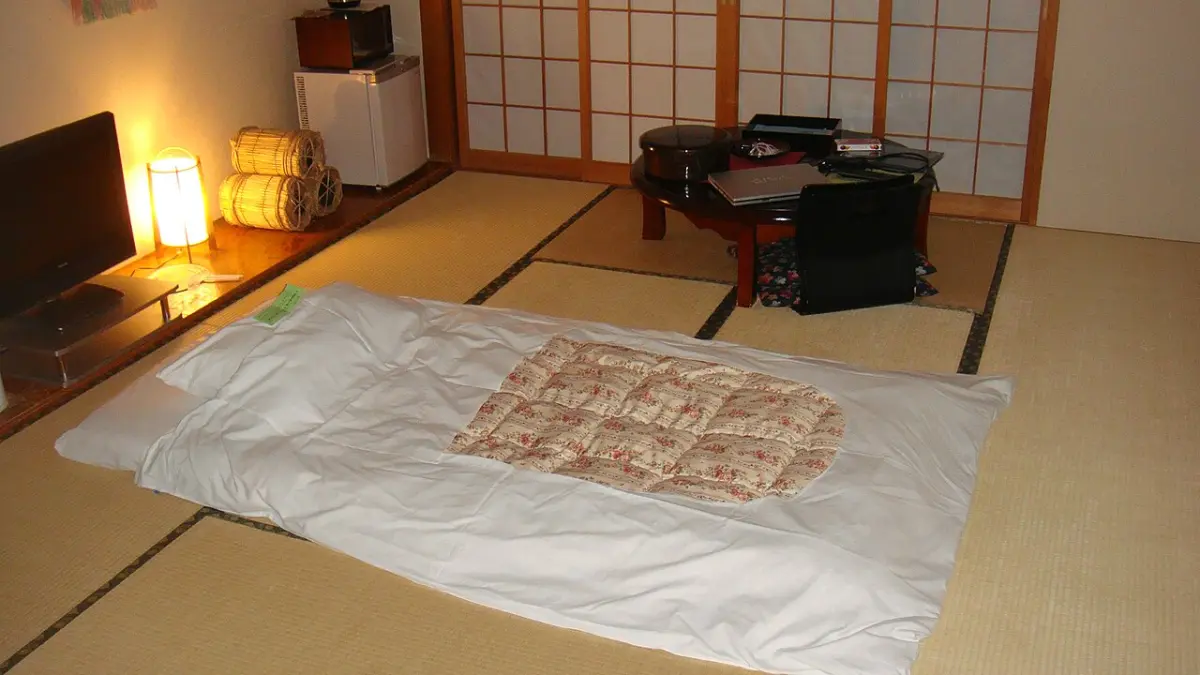 Single futon laid out on tatami in a ryokan room, with a low table and floor lamp