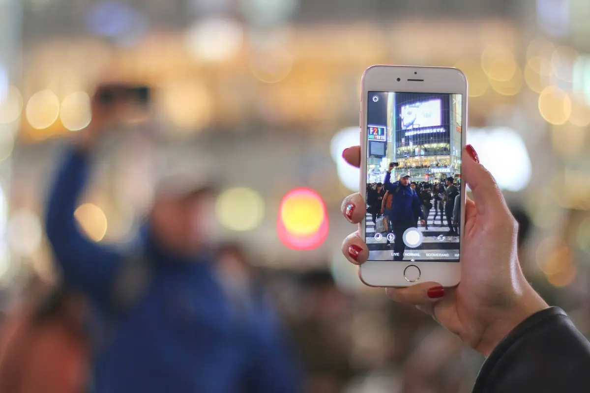 Hand holding a smartphone filming the busy Shibuya Crossing at night in Tokyo