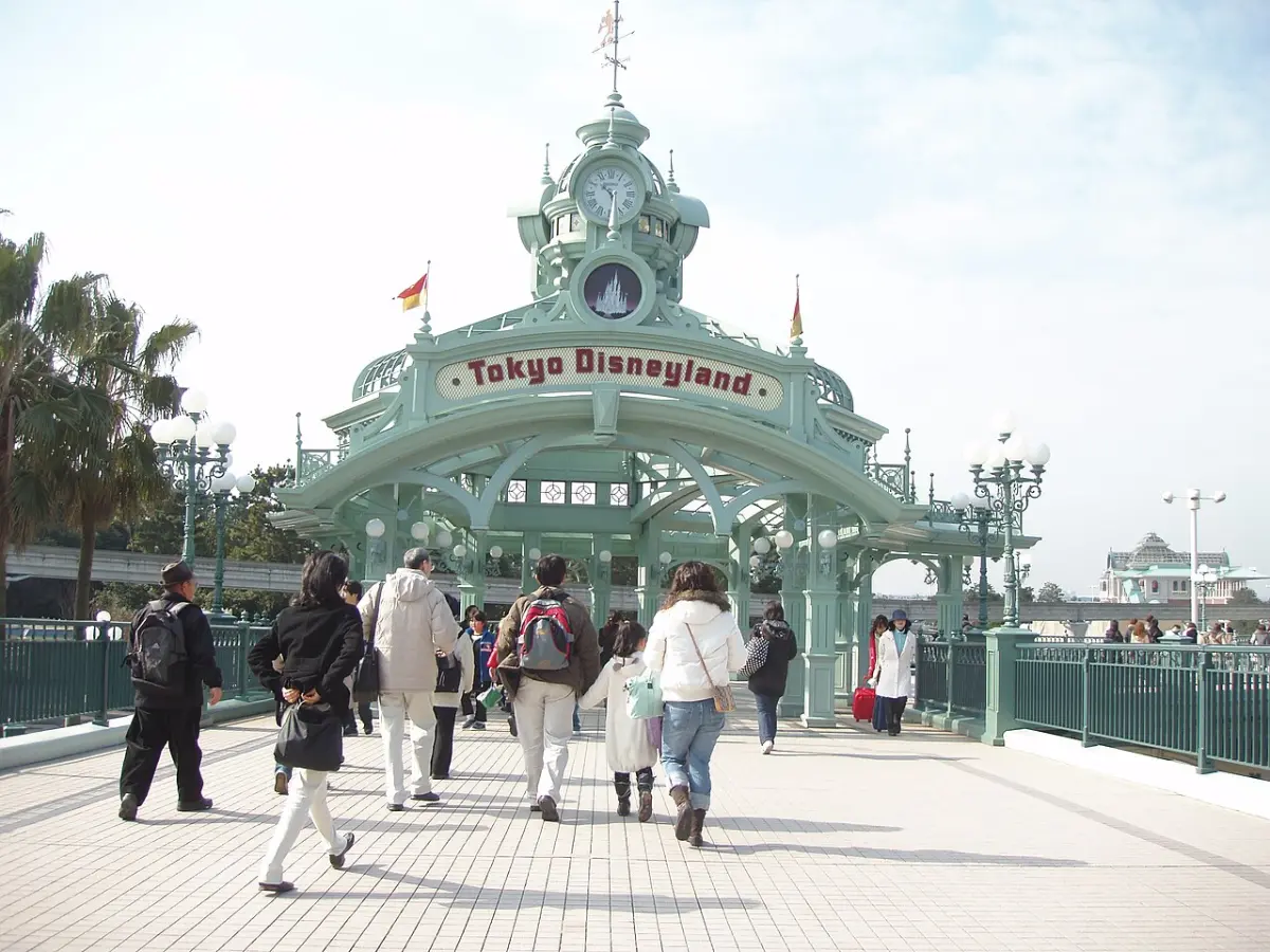 Visitors walking toward the Tokyo Disneyland entrance arch on the walkway from Maihama Station