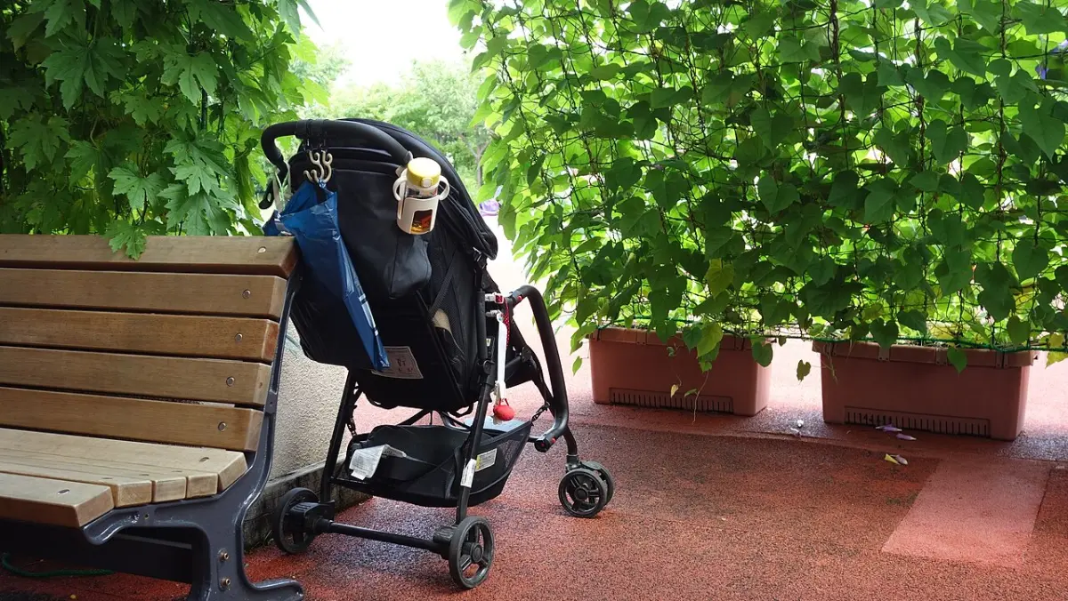 Lightweight baby stroller parked beside a park bench under green vines in Japan